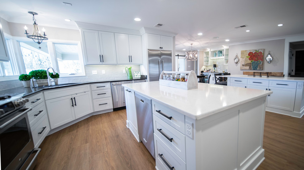 Large minimalist l-shaped medium tone wood floor and brown floor eat-in kitchen photo with an undermount sink, recessed-panel cabinets, white cabinets, solid surface countertops, gray backsplash, stainless steel appliances, two islands and multicolored countertops
