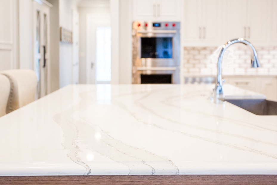 Example of a large transitional u-shaped medium tone wood floor and brown floor eat-in kitchen design in Atlanta with a farmhouse sink, raised-panel cabinets, white cabinets, quartz countertops, white backsplash, brick backsplash, stainless steel appliances, an island and white countertops