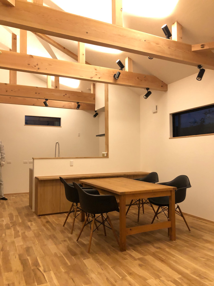 Cette photo montre une salle à manger moderne avec un mur blanc, un sol en bois brun et poutres apparentes.