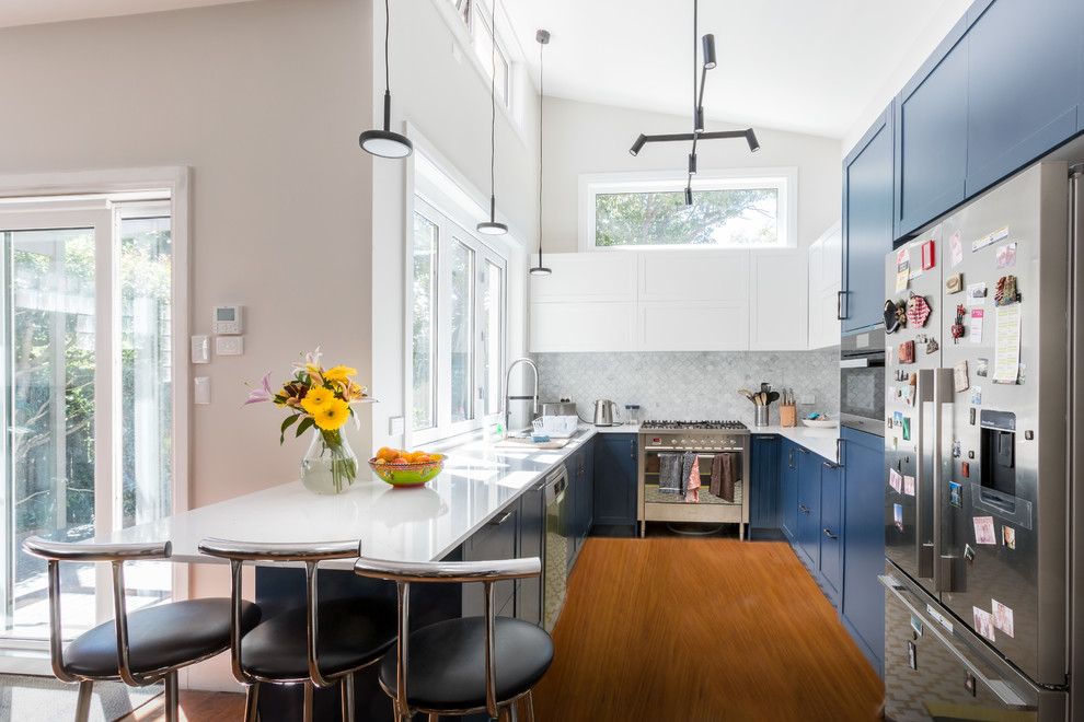 Inspiration for a contemporary u-shaped kitchen in Sydney with an undermount sink, shaker cabinets, blue cabinets, grey splashback, marble splashback, stainless steel appliances, medium hardwood floors, a peninsula, brown floor and white benchtop.