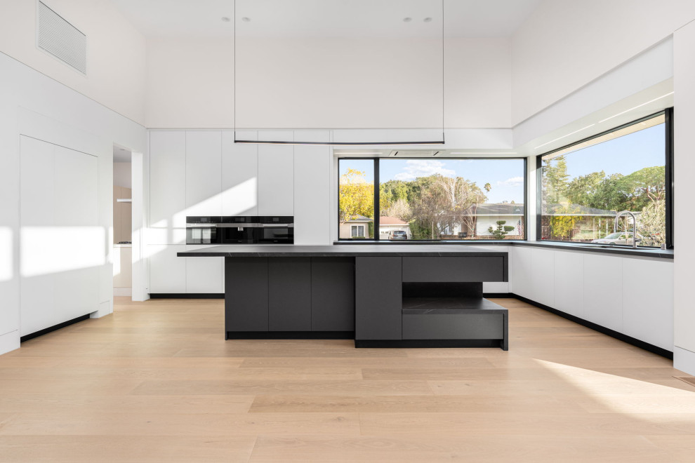 This is an example of a large modern galley open plan kitchen in San Francisco with an undermount sink, flat-panel cabinets, white cabinets, quartz benchtops, black appliances, with island and black benchtop.