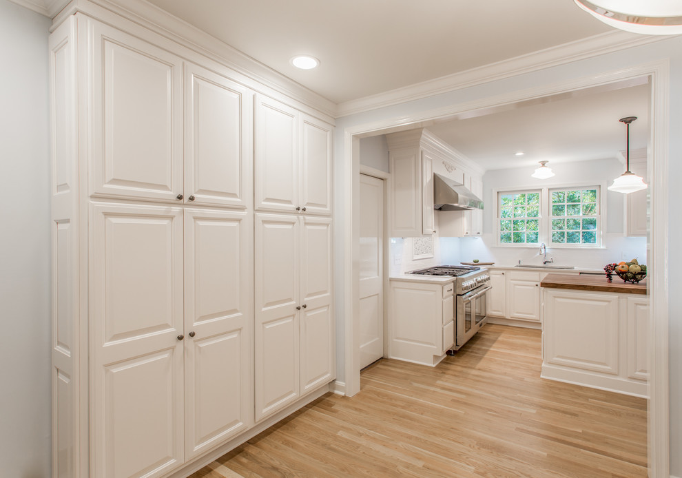 Design ideas for a traditional kitchen in Jacksonville with a double-bowl sink, white cabinets, quartz benchtops, white splashback, subway tile splashback, stainless steel appliances, light hardwood floors, with island and raised-panel cabinets.