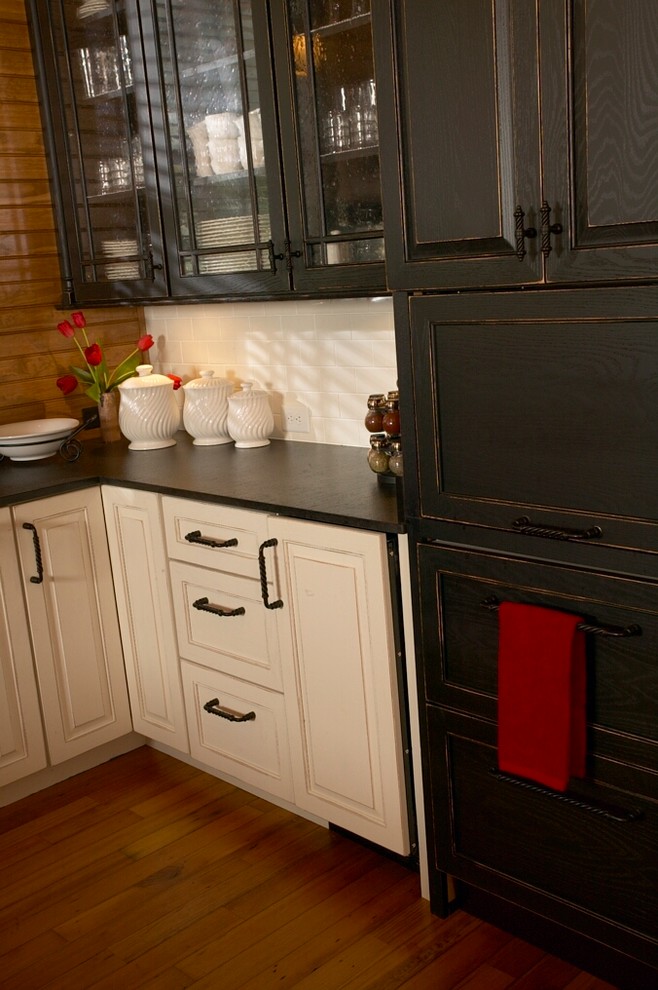 This is an example of a country u-shaped kitchen in Other with a farmhouse sink, raised-panel cabinets, white splashback, panelled appliances, medium hardwood floors, no island and black cabinets.