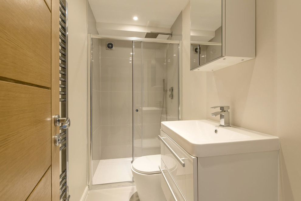 Photo of a large modern master bathroom in London with flat-panel cabinets, white cabinets, a drop-in tub, an open shower, a wall-mount toilet, white tile, ceramic tile, grey walls, bamboo floors, a pedestal sink, tile benchtops, brown floor, a sliding shower screen and white benchtops.