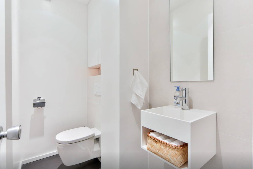 This is an example of a mid-sized contemporary powder room in Paris with white cabinets, a wall-mount toilet, white tile, ceramic tile, white walls, concrete floors, a wall-mount sink and open cabinets.