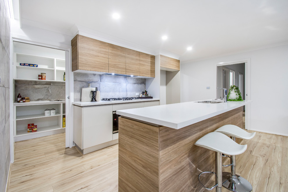 Design ideas for a contemporary galley kitchen in Canberra - Queanbeyan with a double-bowl sink, flat-panel cabinets, light wood cabinets, grey splashback, light hardwood floors, with island, beige floor and white benchtop.