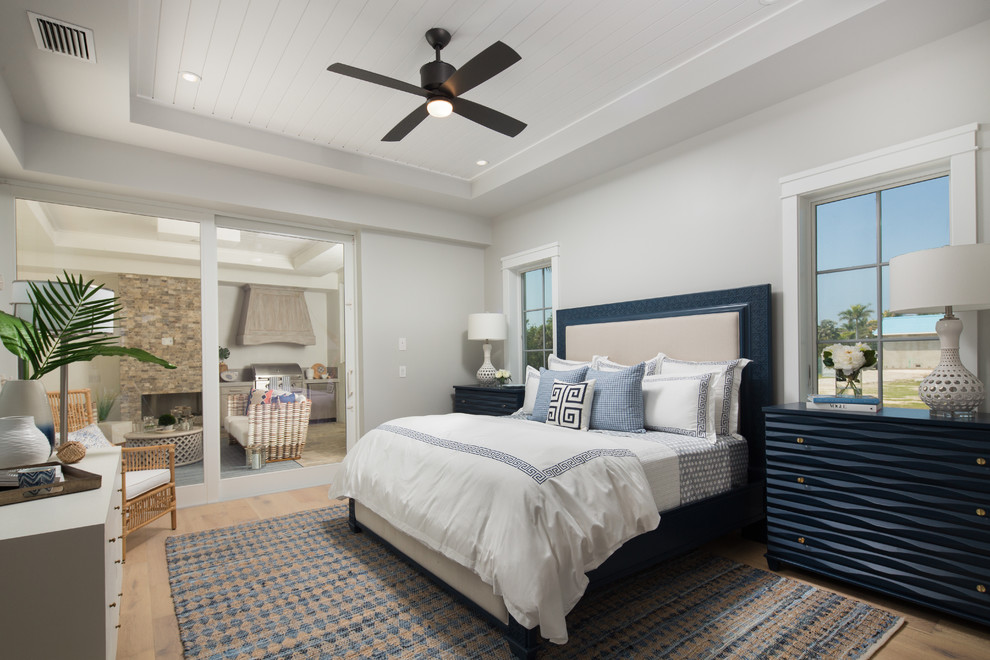 Large beach style master bedroom in Miami with grey walls and light hardwood floors.