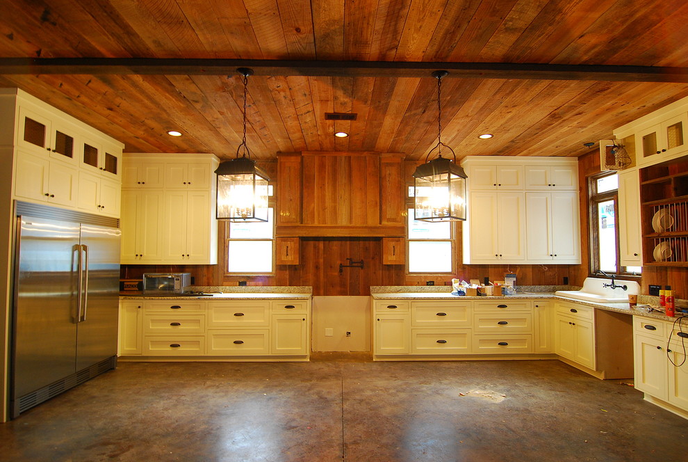Example of a large mountain style u-shaped concrete floor and brown floor kitchen design with a drop-in sink, shaker cabinets, white cabinets, granite countertops, brown backsplash, wood backsplash, stainless steel appliances and no island