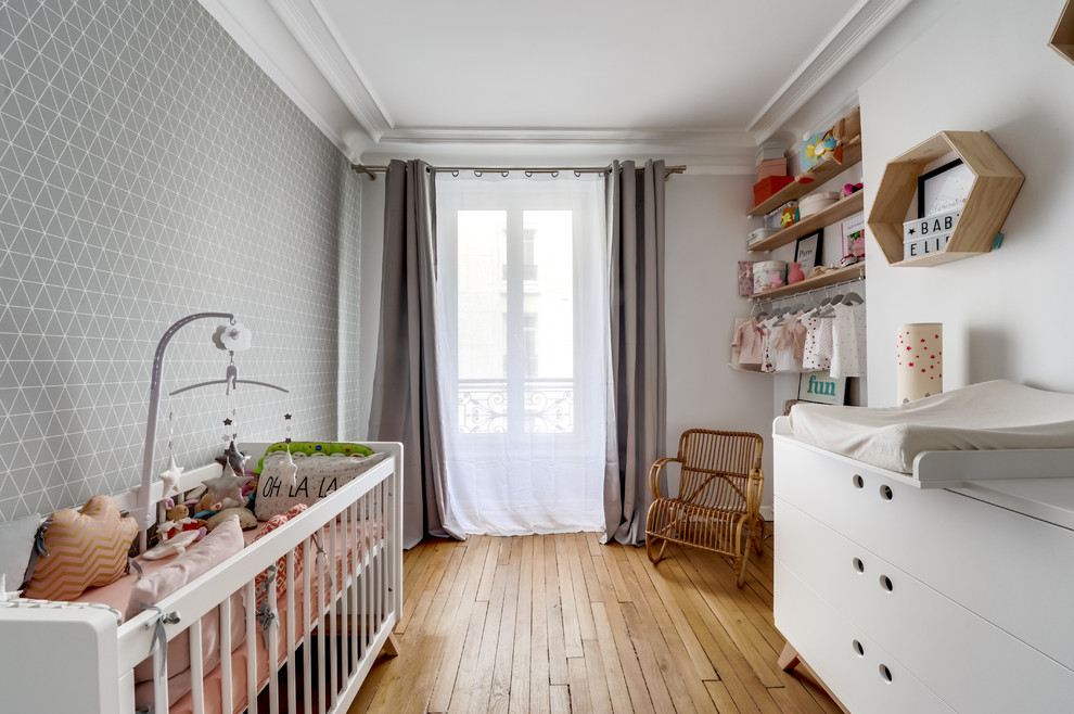 Photo of a mid-sized scandinavian nursery for girls in Paris with grey walls and light hardwood floors.