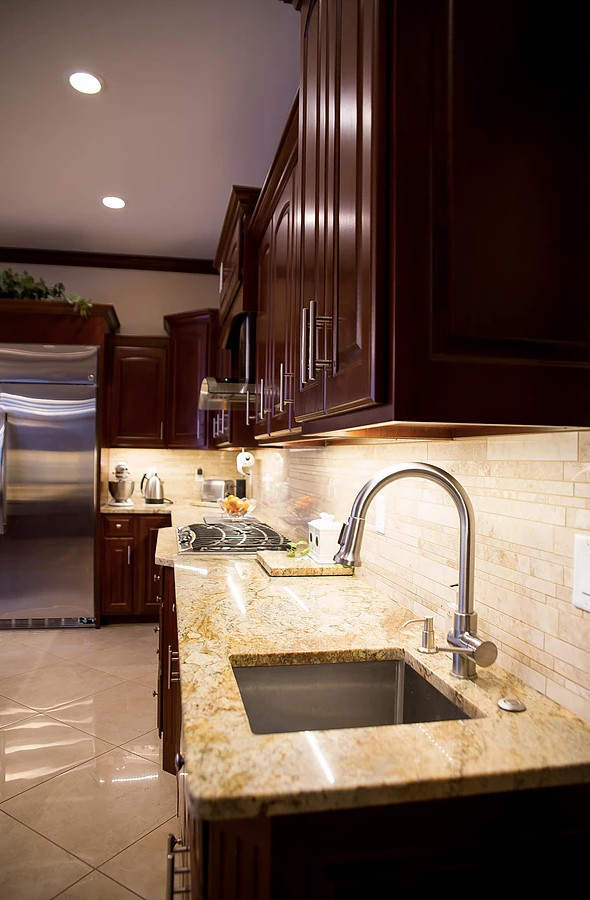 Large minimalist u-shaped porcelain tile and beige floor open concept kitchen photo with an undermount sink, raised-panel cabinets, dark wood cabinets, granite countertops, beige backsplash, matchstick tile backsplash, stainless steel appliances, an island and multicolored countertops