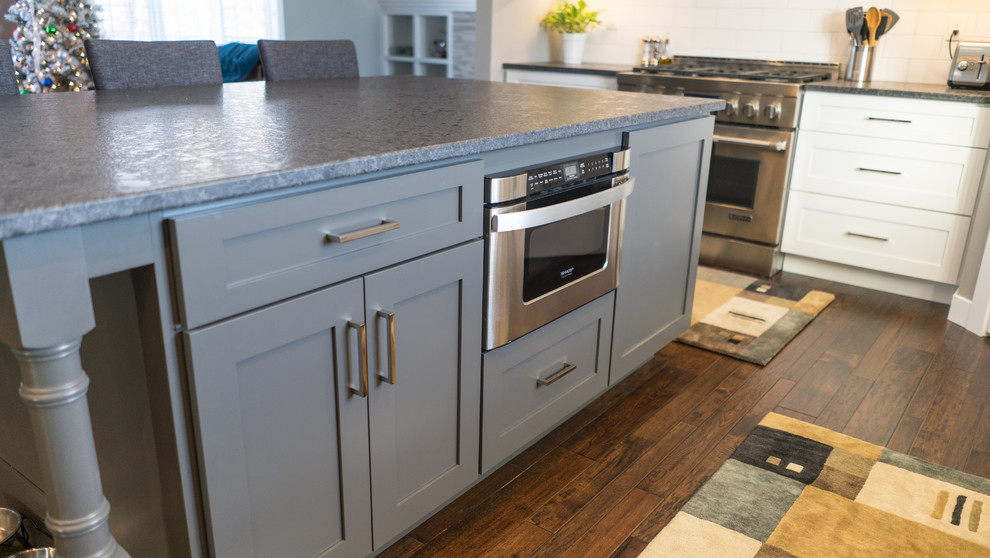 Example of a large transitional u-shaped eat-in kitchen design with a farmhouse sink, flat-panel cabinets, white cabinets, granite countertops, white backsplash, ceramic backsplash, stainless steel appliances and an island