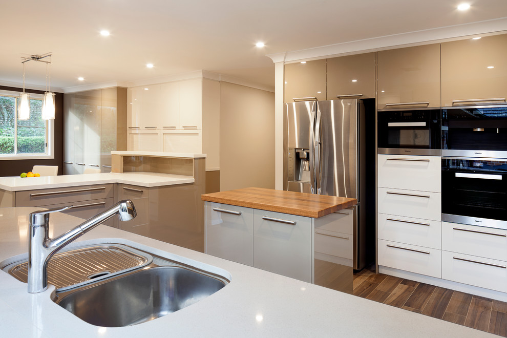 Expansive contemporary u-shaped eat-in kitchen in Sydney with an undermount sink, flat-panel cabinets, green cabinets, quartz benchtops, brown splashback, glass sheet splashback, stainless steel appliances, ceramic floors and multiple islands.