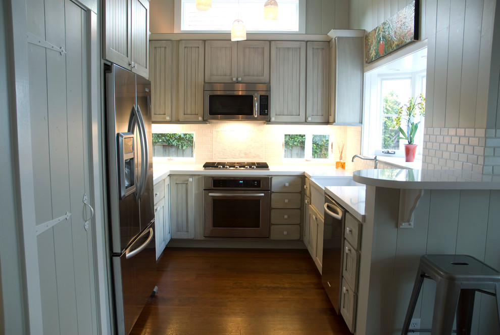 Photo of a small traditional u-shaped eat-in kitchen in San Francisco with a farmhouse sink, louvered cabinets, grey cabinets, quartz benchtops, white splashback, porcelain splashback, stainless steel appliances, medium hardwood floors, no island and brown floor.