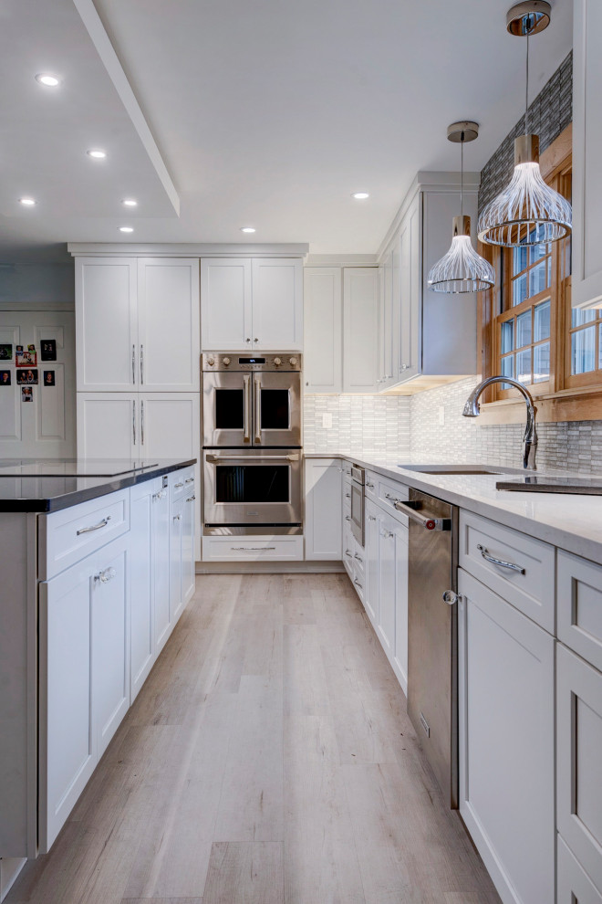 Inspiration for a large transitional u-shaped light wood floor and beige floor open concept kitchen remodel in New York with an undermount sink, shaker cabinets, white cabinets, quartzite countertops, white backsplash, ceramic backsplash, stainless steel appliances, an island and white countertops