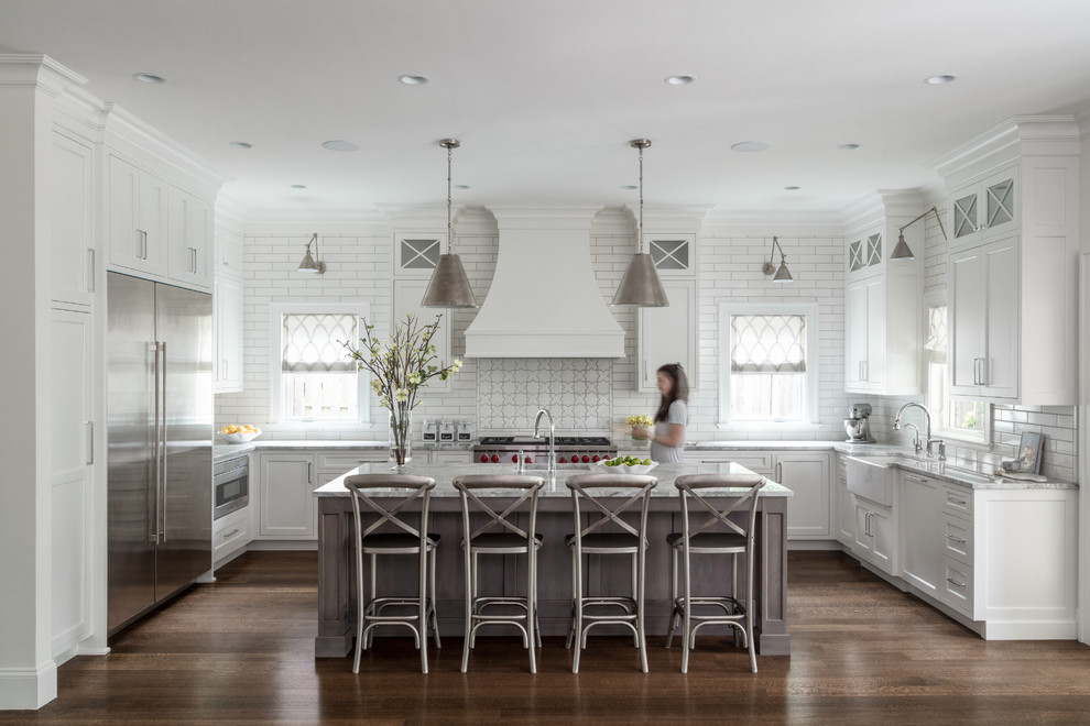 Inspiration for a transitional u-shaped kitchen in New York with a farmhouse sink, shaker cabinets, white cabinets, white splashback, subway tile splashback, stainless steel appliances, dark hardwood floors, with island, brown floor and grey benchtop.