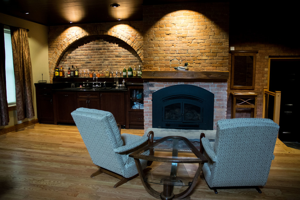 This is an example of a large industrial loft-style family room in New York with a home bar, beige walls, light hardwood floors, a standard fireplace, a brick fireplace surround and a wall-mounted tv.