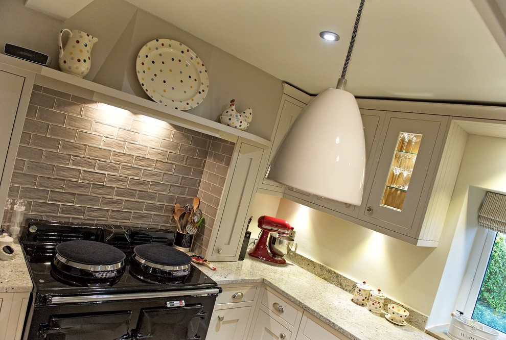 Photo of a large traditional l-shaped eat-in kitchen in Manchester with a farmhouse sink, recessed-panel cabinets, beige cabinets, granite benchtops, brown splashback, porcelain splashback, stainless steel appliances, limestone floors and with island.