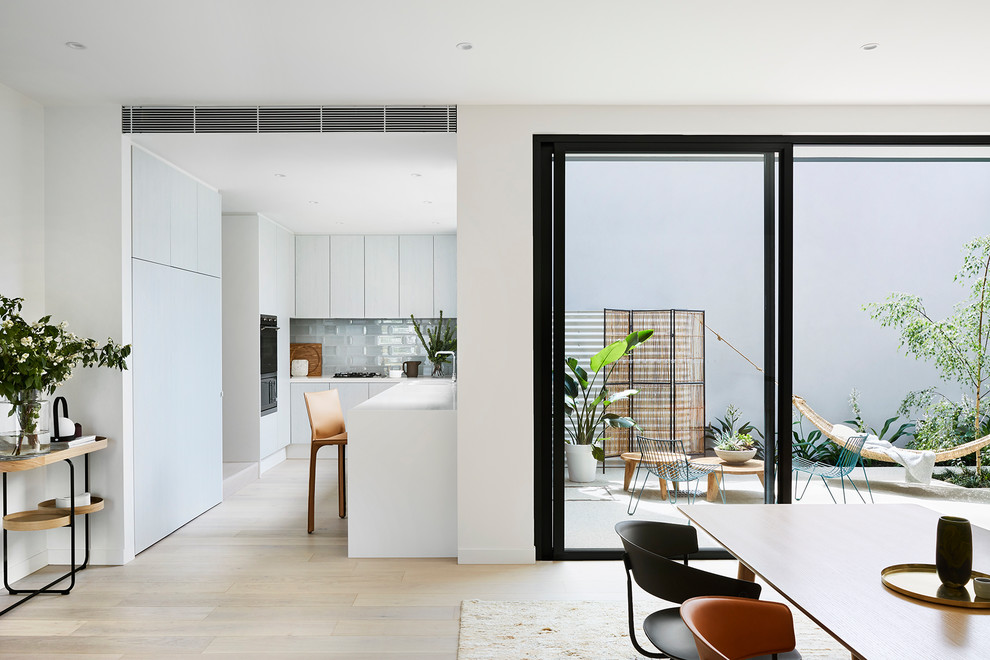 Mid-sized contemporary u-shaped open plan kitchen in Melbourne with an undermount sink, grey splashback, ceramic splashback, light hardwood floors, white benchtop and black appliances.