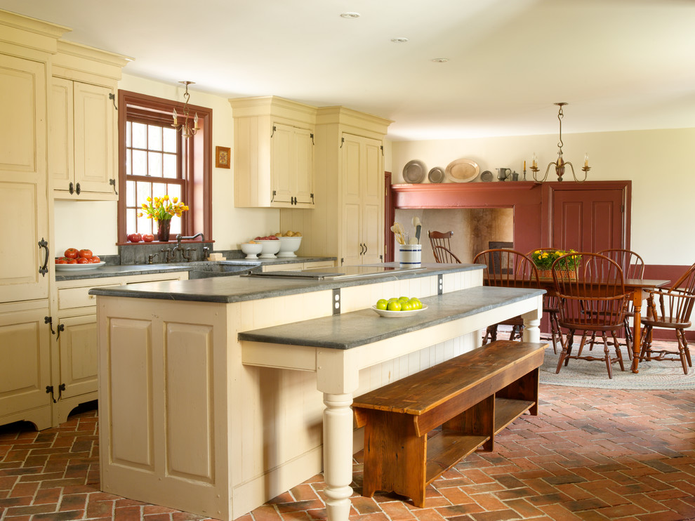 Photo of a mid-sized country single-wall eat-in kitchen in Philadelphia with raised-panel cabinets, beige cabinets, brick floors, with island, a farmhouse sink, panelled appliances, red floor, concrete benchtops and grey benchtop.
