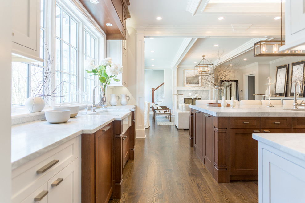 This is an example of an expansive transitional u-shaped open plan kitchen in New York with a farmhouse sink, recessed-panel cabinets, medium wood cabinets, granite benchtops, white splashback, ceramic splashback, panelled appliances, medium hardwood floors and with island.