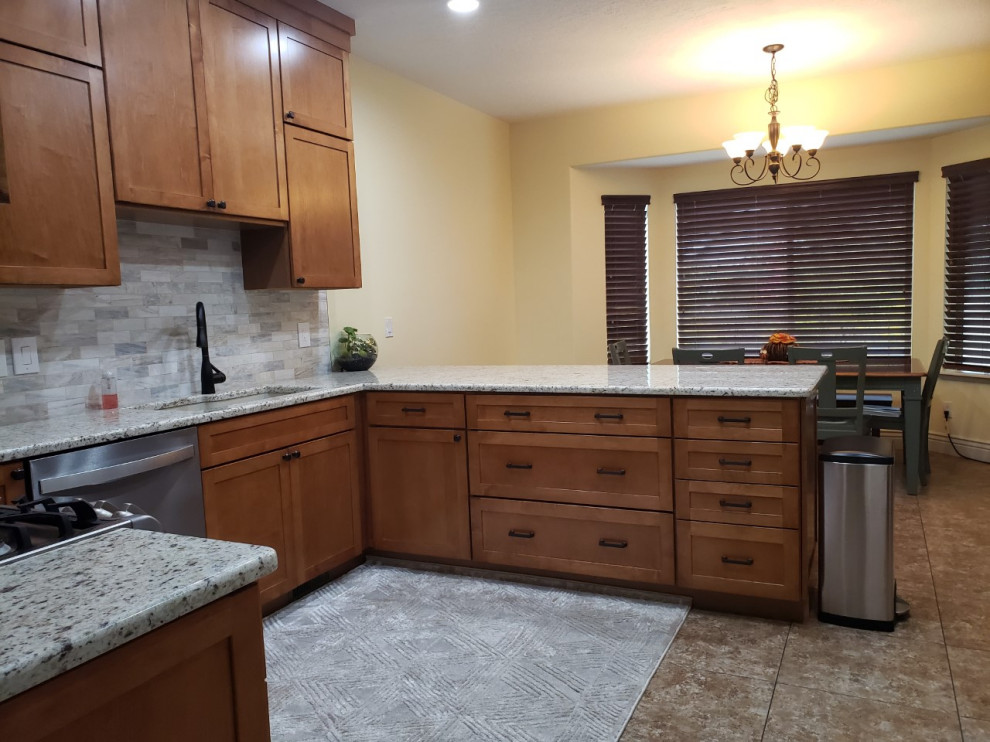 Photo of a medium sized traditional u-shaped kitchen/diner in Salt Lake City with a submerged sink, shaker cabinets, brown cabinets, granite worktops, grey splashback, stone tiled splashback, stainless steel appliances, porcelain flooring, a breakfast bar, brown floors and beige worktops.