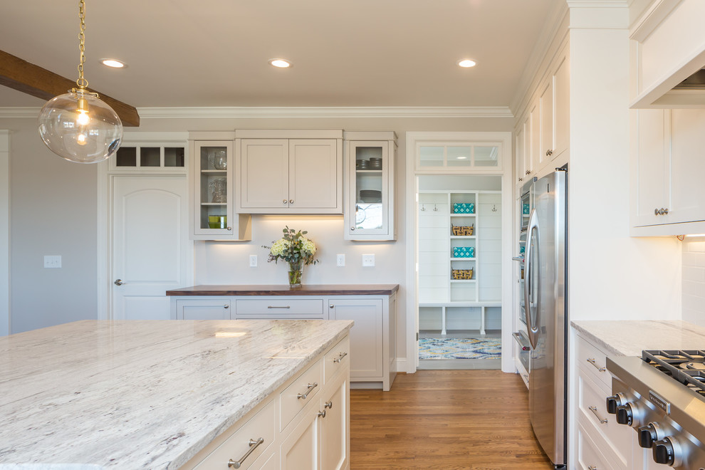 Photo of a large transitional u-shaped eat-in kitchen in Raleigh with a farmhouse sink, shaker cabinets, white cabinets, white splashback, stainless steel appliances, medium hardwood floors, with island, brown floor, quartzite benchtops, subway tile splashback and white benchtop.