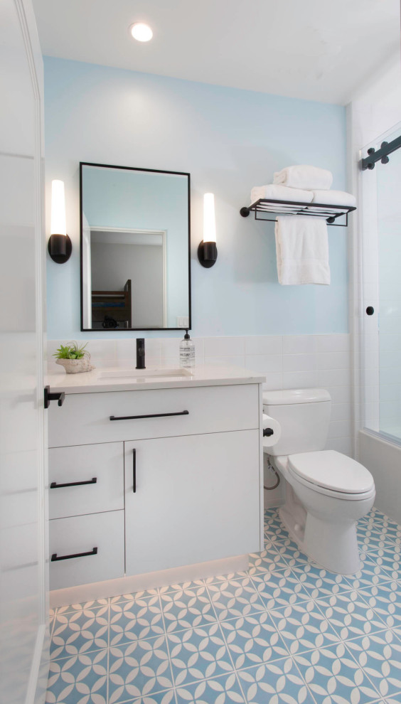 This is an example of a small beach style kids bathroom in San Diego with flat-panel cabinets, white cabinets, an alcove tub, a shower/bathtub combo, a two-piece toilet, white tile, ceramic tile, blue walls, cement tiles, an undermount sink, engineered quartz benchtops, blue floor, a sliding shower screen, white benchtops, a niche, a single vanity and a built-in vanity.