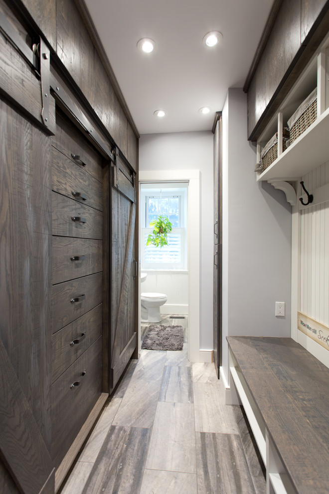 Photo of a mid-sized beach style gender-neutral walk-in wardrobe in Toronto with dark wood cabinets, porcelain floors and flat-panel cabinets.