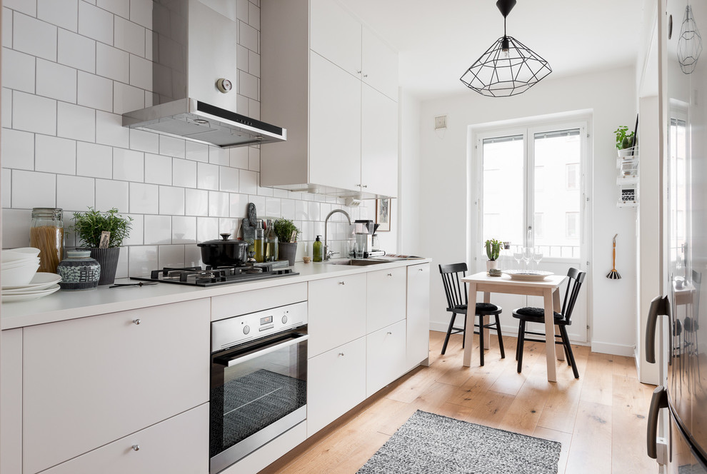 Mid-sized scandinavian single-wall open plan kitchen in Gothenburg with a drop-in sink, flat-panel cabinets, white cabinets, laminate benchtops, white splashback, porcelain splashback, stainless steel appliances, medium hardwood floors and no island.