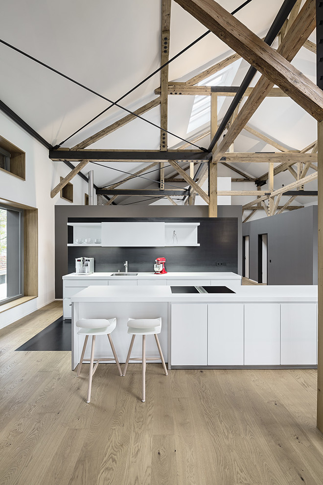 Design ideas for a contemporary galley open plan kitchen in Munich with a drop-in sink, flat-panel cabinets, white cabinets, black splashback and light hardwood floors.
