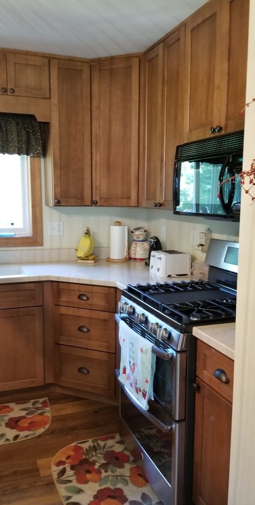 Example of a transitional l-shaped eat-in kitchen design with a double-bowl sink, shaker cabinets, solid surface countertops, stainless steel appliances and an island