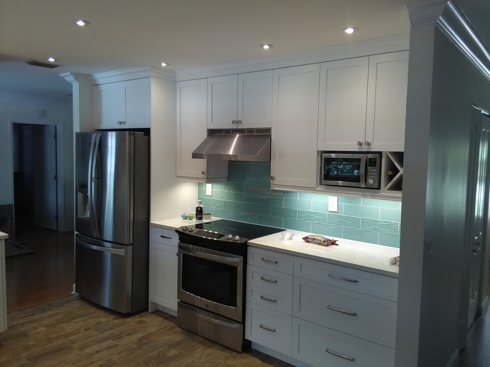 This is an example of a mid-sized beach style l-shaped eat-in kitchen in Miami with a double-bowl sink, shaker cabinets, white cabinets, quartz benchtops, blue splashback, glass tile splashback, stainless steel appliances, porcelain floors and no island.
