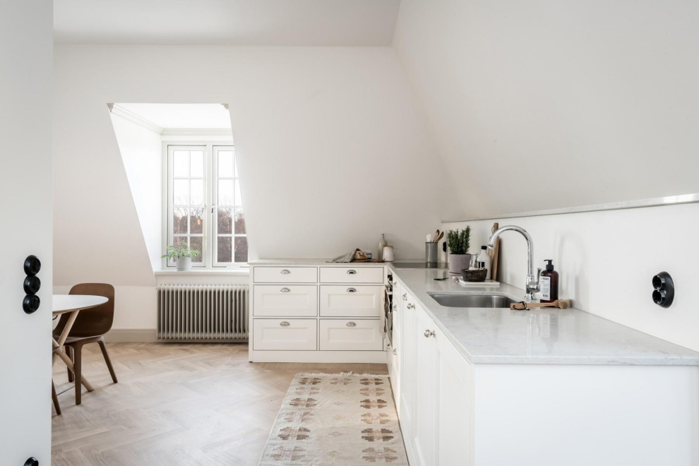 Photo of a scandinavian l-shaped eat-in kitchen in Stockholm with an undermount sink, recessed-panel cabinets, white cabinets, medium hardwood floors, no island, brown floor, grey benchtop and vaulted.