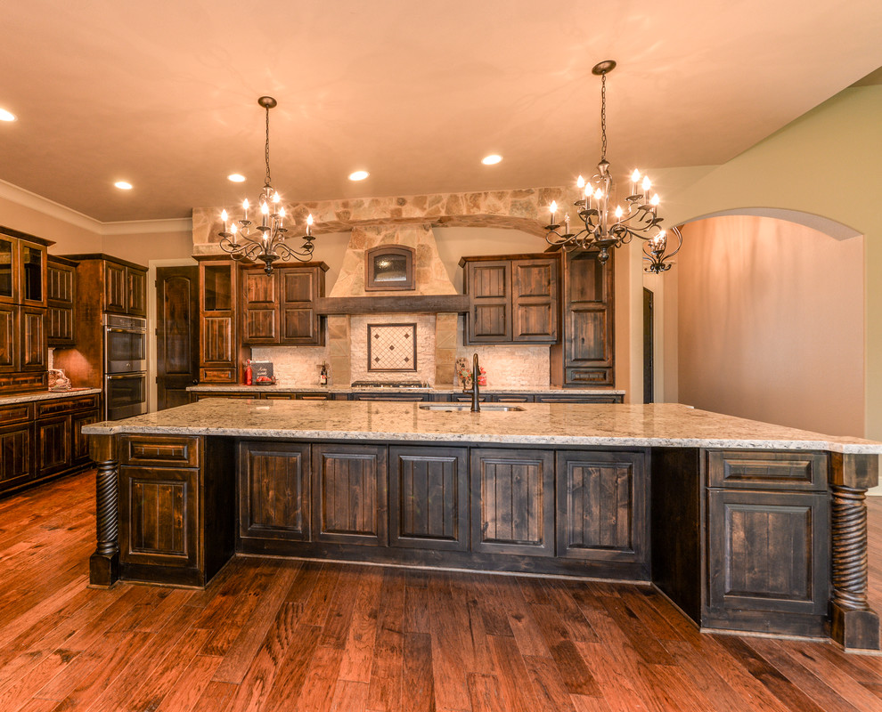 Inspiration for a large country open plan kitchen in Austin with an undermount sink, raised-panel cabinets, dark wood cabinets, granite benchtops, white splashback, stone tile splashback, stainless steel appliances, dark hardwood floors and with island.