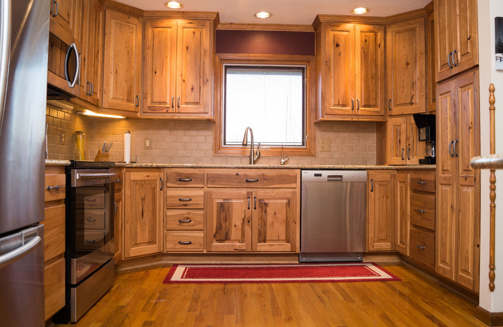 Example of a mid-sized mountain style galley light wood floor eat-in kitchen design with an undermount sink, raised-panel cabinets, light wood cabinets, granite countertops, beige backsplash, ceramic backsplash, stainless steel appliances and no island