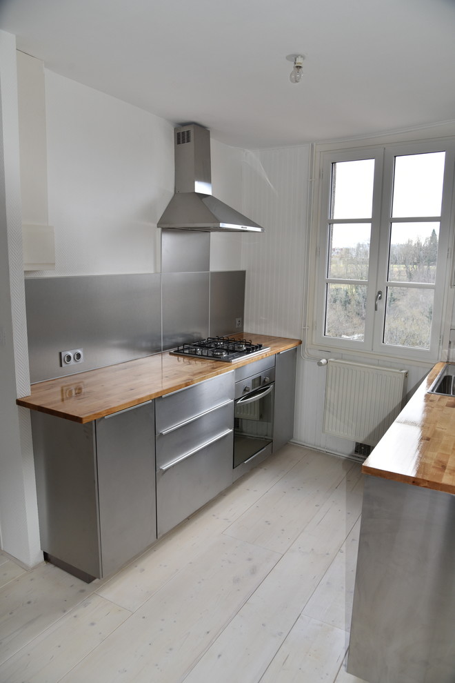 Photo of a mid-sized traditional galley open plan kitchen in Dijon with a single-bowl sink, beaded inset cabinets, stainless steel cabinets, wood benchtops, metallic splashback, timber splashback, stainless steel appliances, light hardwood floors, with island, beige floor and beige benchtop.