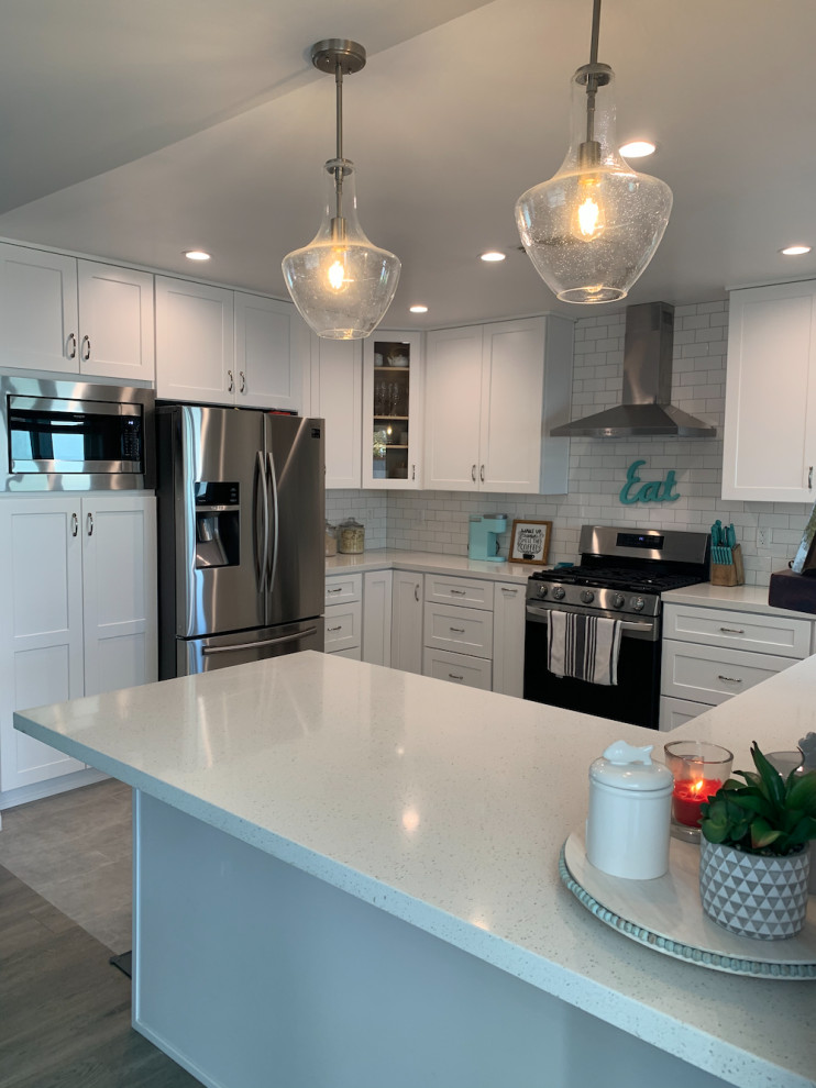 This is an example of a mid-sized modern u-shaped eat-in kitchen in Los Angeles with a drop-in sink, shaker cabinets, white cabinets, quartzite benchtops, white splashback, porcelain splashback, stainless steel appliances, ceramic floors, a peninsula and grey floor.