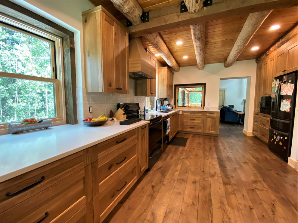 Mid-sized mountain style l-shaped medium tone wood floor, brown floor and exposed beam enclosed kitchen photo in Denver with an undermount sink, shaker cabinets, medium tone wood cabinets, white backsplash, black appliances and white countertops