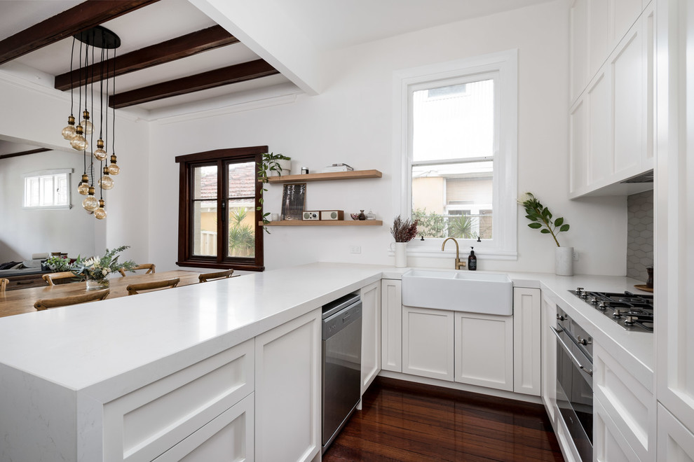 Design ideas for a mid-sized transitional u-shaped open plan kitchen in Perth with a farmhouse sink, recessed-panel cabinets, white cabinets, quartz benchtops, grey splashback, ceramic splashback, white appliances, medium hardwood floors, no island and white benchtop.