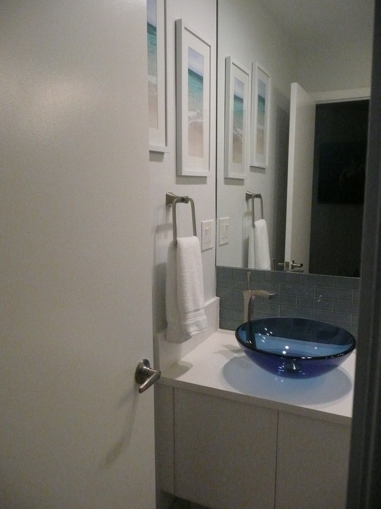 Photo of a mid-sized beach style powder room in Miami with flat-panel cabinets, white cabinets, a one-piece toilet, blue tile, glass tile, white walls, ceramic floors, a vessel sink, engineered quartz benchtops and white benchtops.