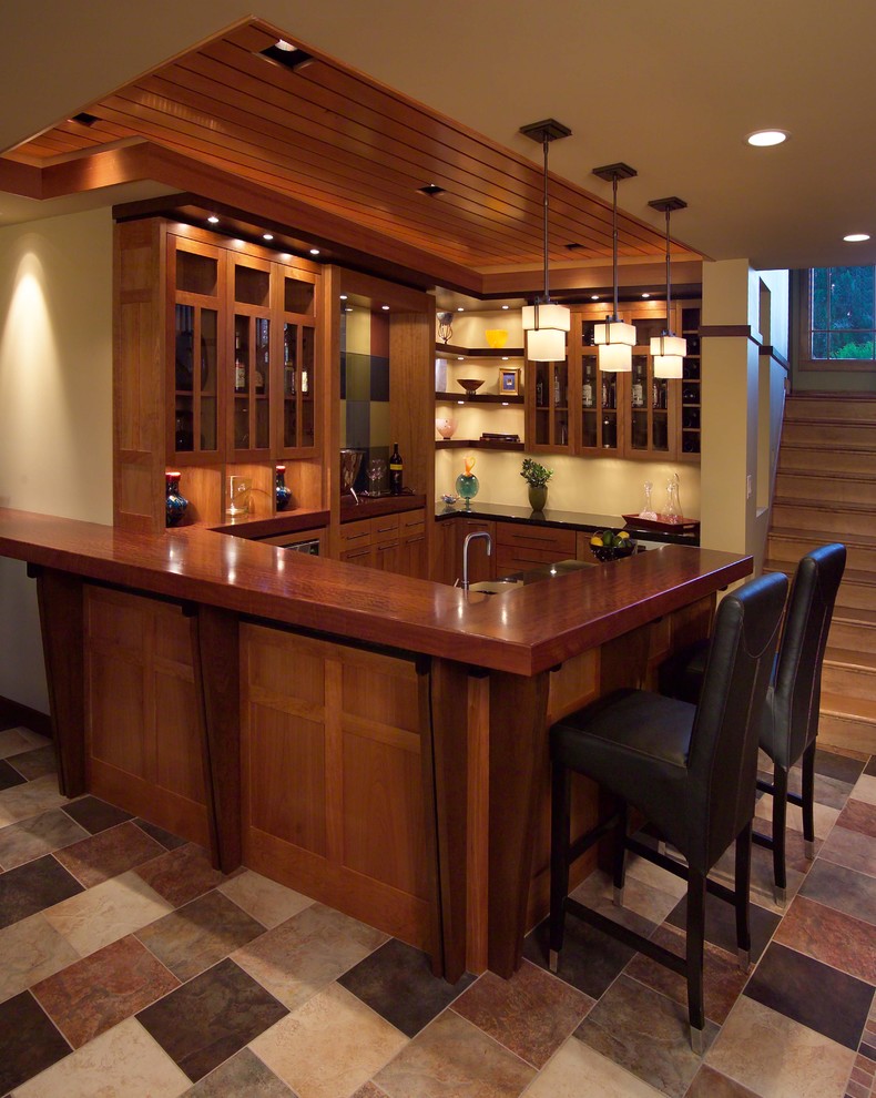 Photo of a mid-sized arts and crafts u-shaped seated home bar in Minneapolis with ceramic floors, glass-front cabinets, medium wood cabinets, wood benchtops, multi-coloured floor and brown benchtop.
