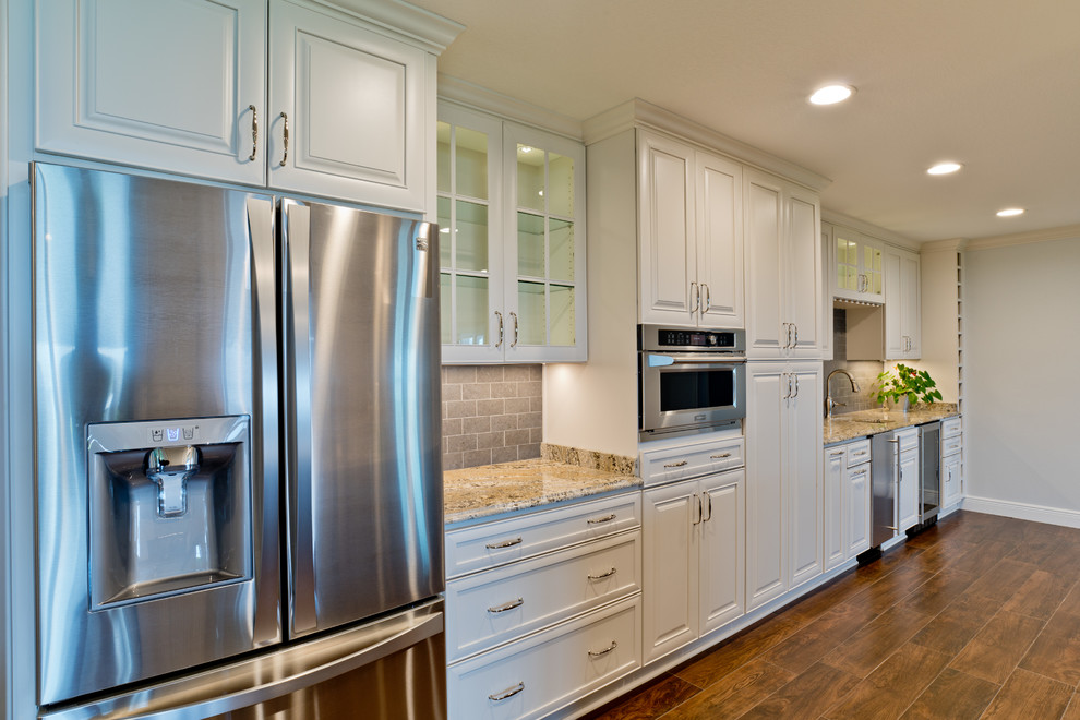 Large transitional galley porcelain tile eat-in kitchen photo in Miami with an undermount sink, raised-panel cabinets, white cabinets, granite countertops, gray backsplash, porcelain backsplash, stainless steel appliances and an island