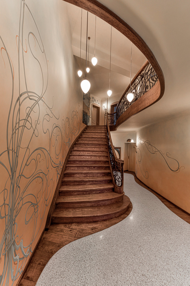 На фото: изогнутая деревянная лестница в классическом стиле с деревянными ступенями и металлическими перилами с