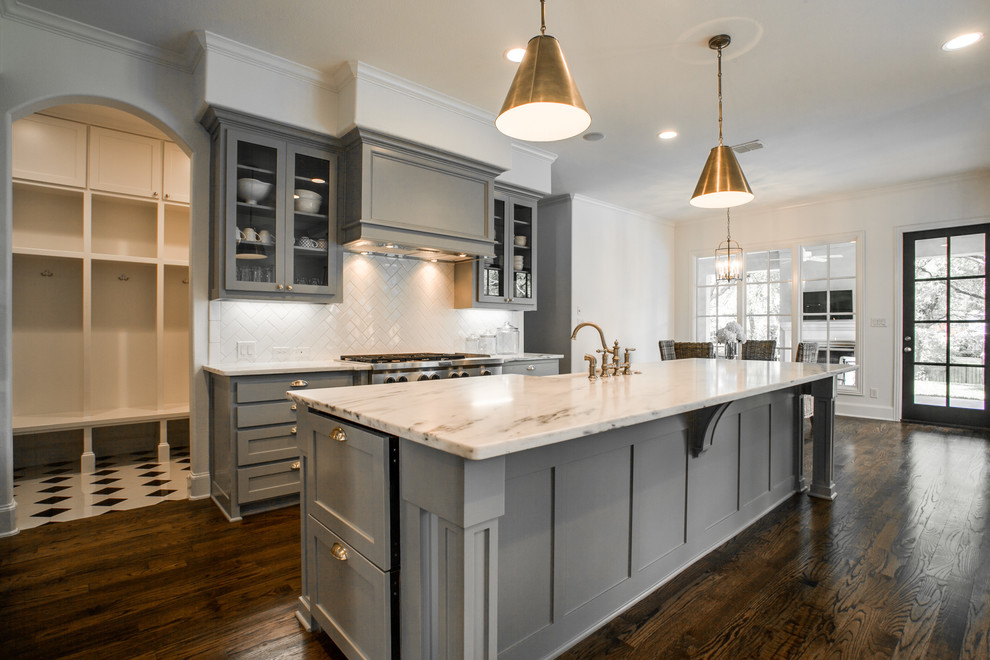 Inspiration for a mid-sized transitional galley dark wood floor and brown floor eat-in kitchen remodel in Dallas with a farmhouse sink, shaker cabinets, gray cabinets, marble countertops, white backsplash, ceramic backsplash, stainless steel appliances and an island