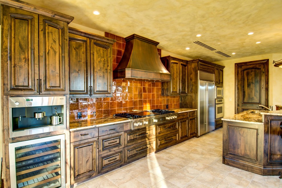 Photo of a mid-sized mediterranean galley open plan kitchen in Salt Lake City with an undermount sink, raised-panel cabinets, dark wood cabinets, granite benchtops, brown splashback, ceramic splashback, stainless steel appliances, ceramic floors and with island.