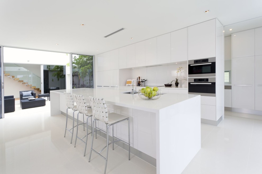 Inspiration for a contemporary galley kitchen in Los Angeles with an undermount sink, flat-panel cabinets, white cabinets, white splashback, stainless steel appliances and with island.