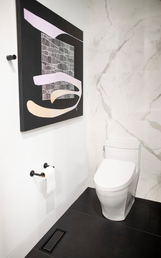 Design ideas for a mid-sized modern powder room in Toronto with a one-piece toilet, white tile, marble, white walls, porcelain floors, solid surface benchtops, black floor and white benchtops.