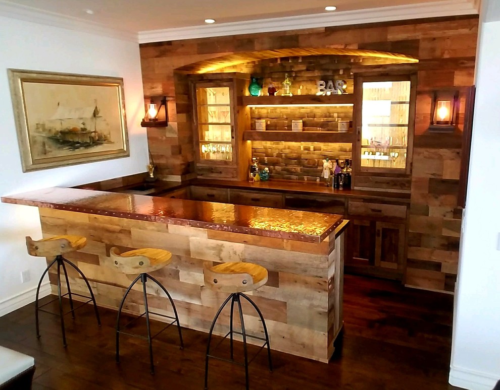 Photo of a mid-sized country u-shaped seated home bar in Orange County with a drop-in sink, shaker cabinets, distressed cabinets, copper benchtops, brown splashback, timber splashback, dark hardwood floors and brown floor.