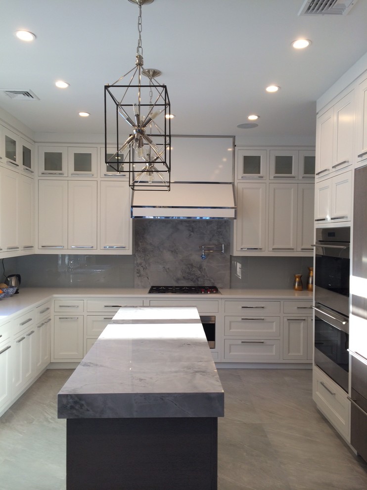 Example of a large transitional l-shaped kitchen design in New York with shaker cabinets, white cabinets, gray backsplash, glass sheet backsplash, stainless steel appliances and an island