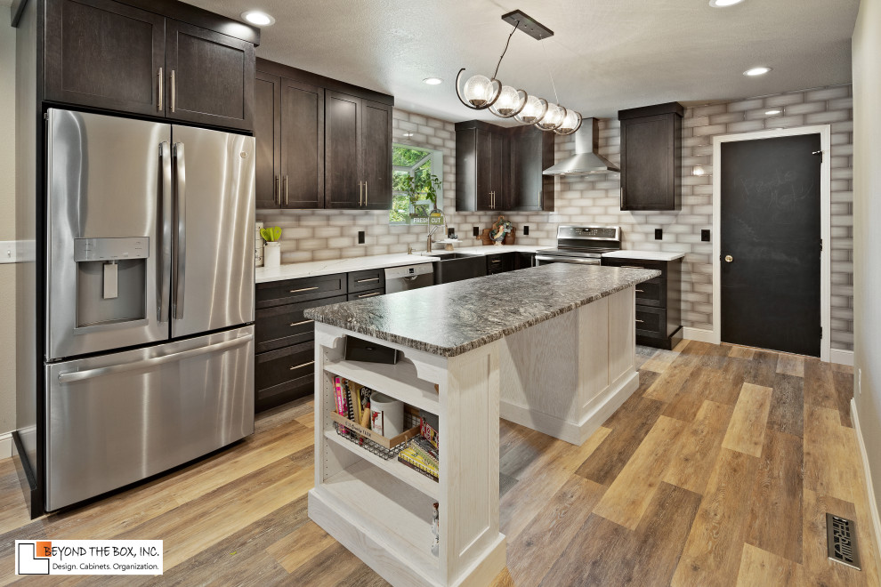 Inspiration for a mid-sized transitional l-shaped medium tone wood floor and brown floor kitchen remodel with a farmhouse sink, shaker cabinets, black cabinets, granite countertops, gray backsplash, ceramic backsplash, stainless steel appliances, an island and white countertops